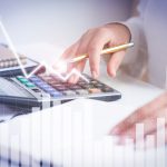 Accountant calculating profit with financial analysis graphs. Notebook, glasses and calculator lying on desk. Accountancy concept. Cropped view.